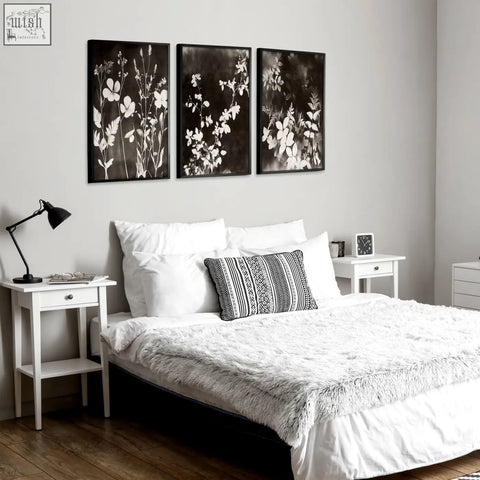 Black-framed dark brown-black nature painting art prints with white floral silhouettes hang above the bed set of 3