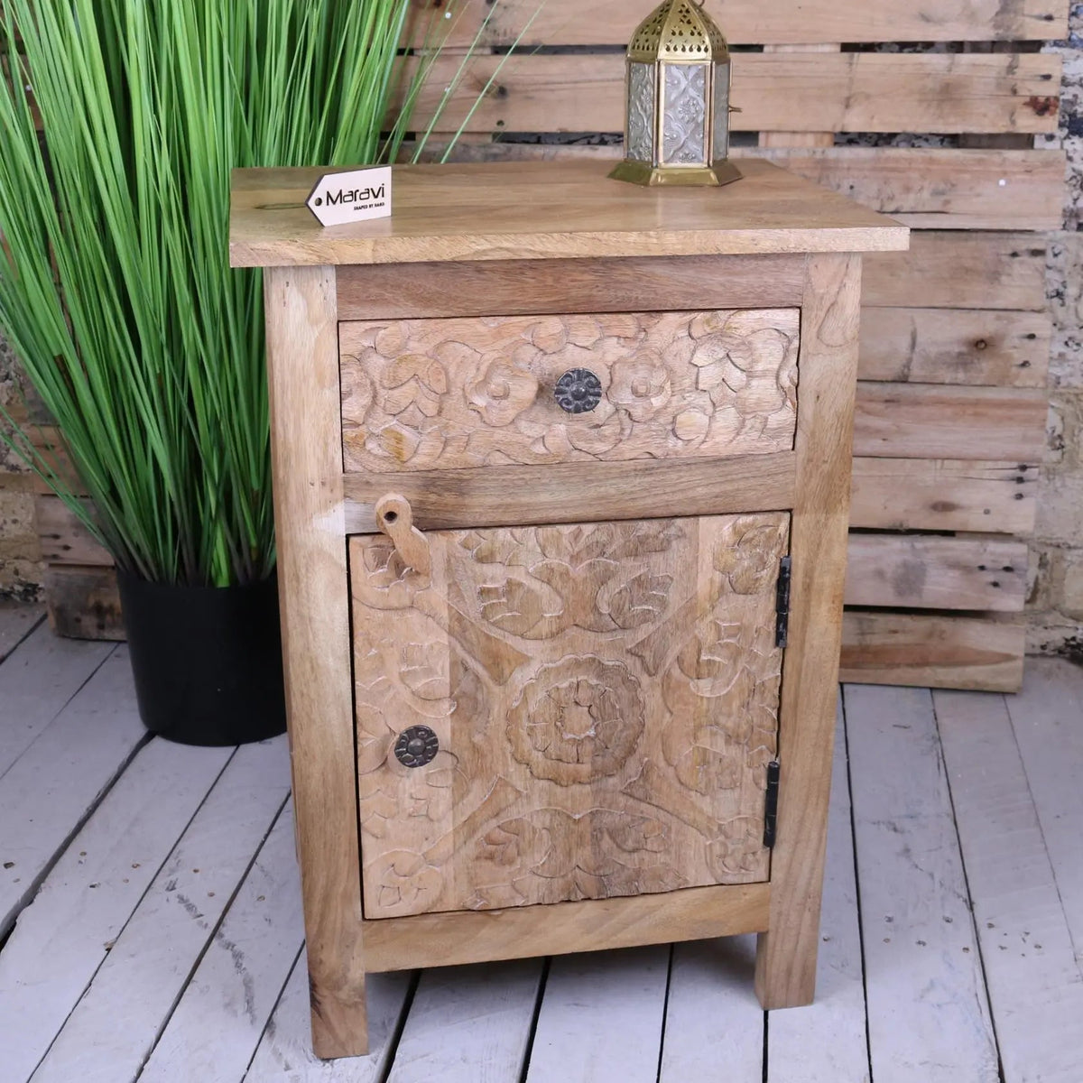 Light-colored mango wood bedside cabinet with intricate floral carvings and dark metal knobs for bedroom use