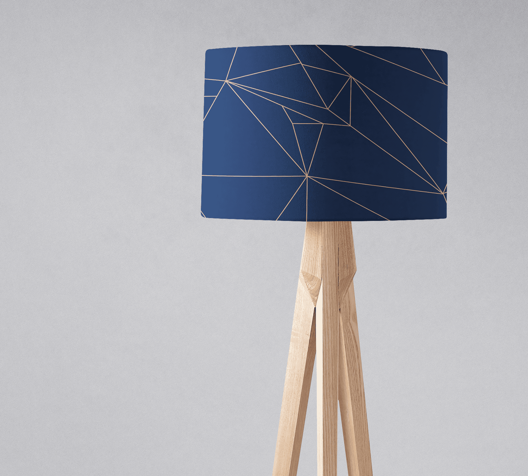 Navy blue table lamp with geometric gold line pattern on lampshade and light wood tripod base