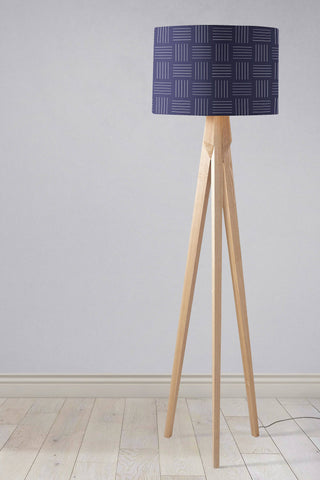 A navy blue table lamp with white lines geometric design lampshade on light wood tripod legs with inch diameter