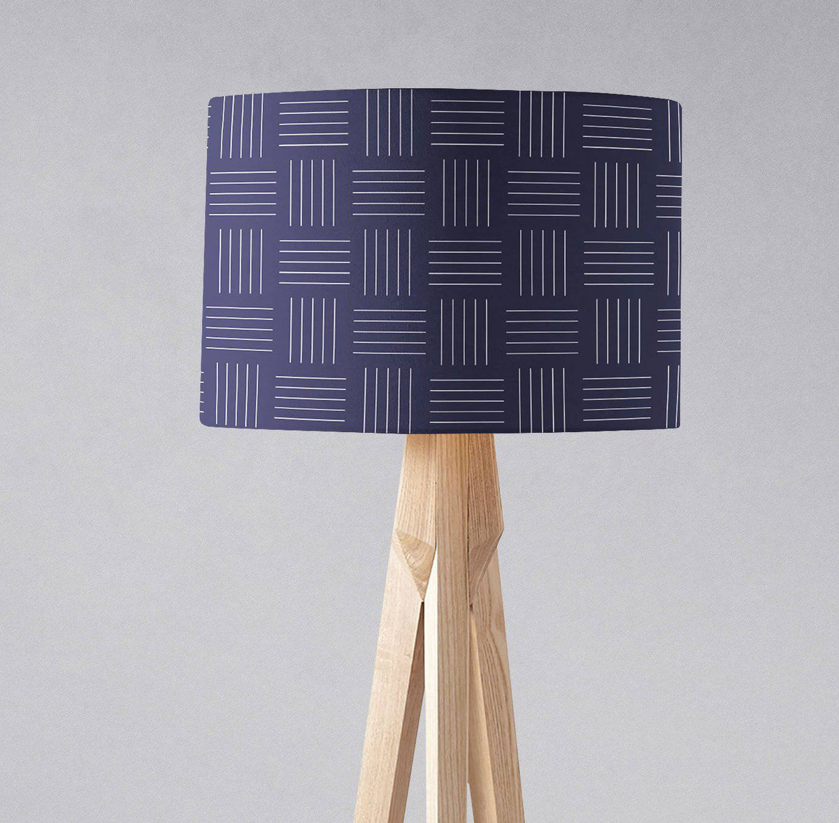 Navy blue table lamp with white geometric lines on a light wood tripod base and inch diameter lampshade