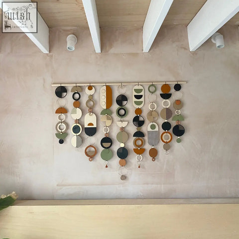 A modern wall art featuring geometric wooden discs in earthy tones like black white beige olive green and mustard yellow
