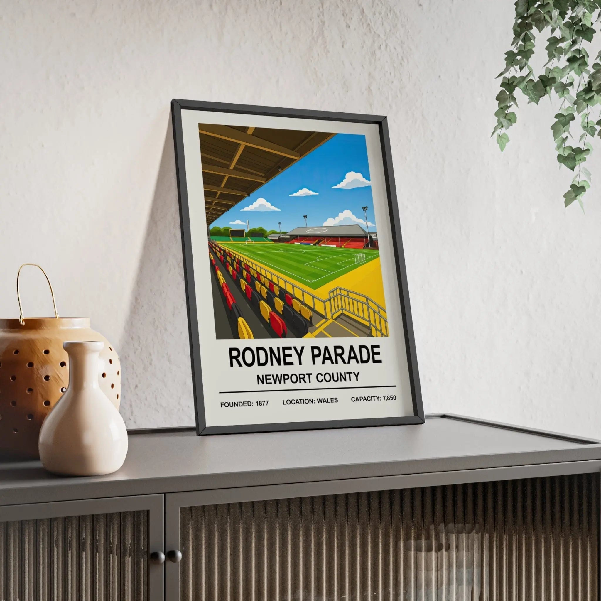 A framed newport rodney parade stadium print showing vibrant green grass, yellow and red seating under blue sky