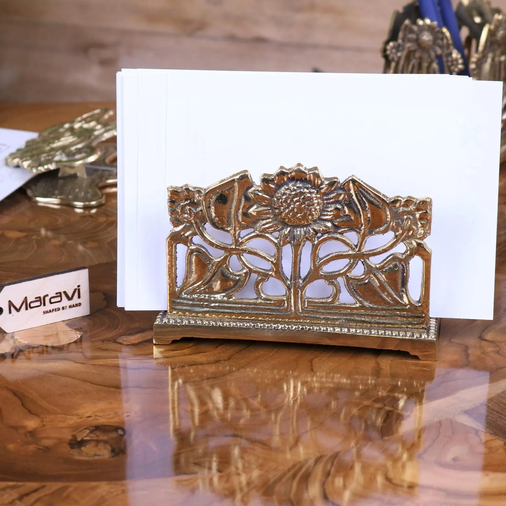 Gold-toned metal card holder with intricate sunflower leaf design on decorative base perfect for luxury desk accessories