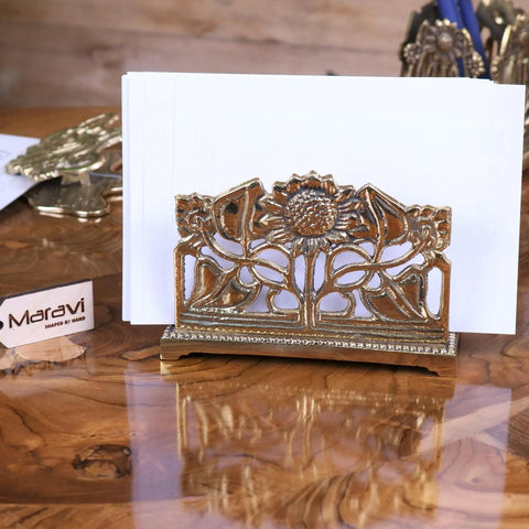 Gold-toned metal card holder with intricate sunflower leaf design on decorative base perfect for luxury desk accessories
