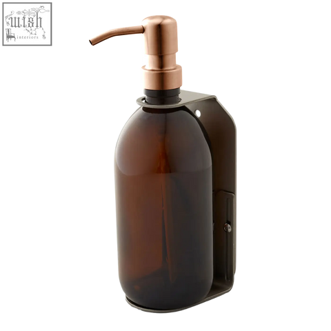 A sleek amber glass wall-mounted soap dispenser with rose gold pump and matte black stainless steel mount