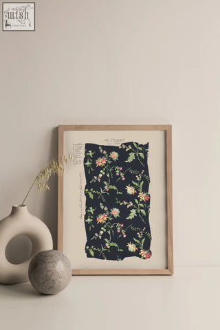 A framed botanical print with midnight blooms vintage pink and green flowers on dark navy fabric in light wood frame