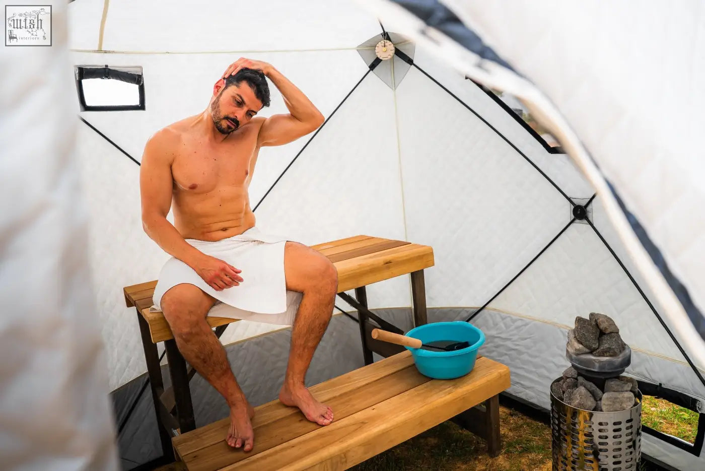 A man in a white towel sits inside the white r14s tent of the noir xxl signature finsteam sauna suite with second tent safety pack