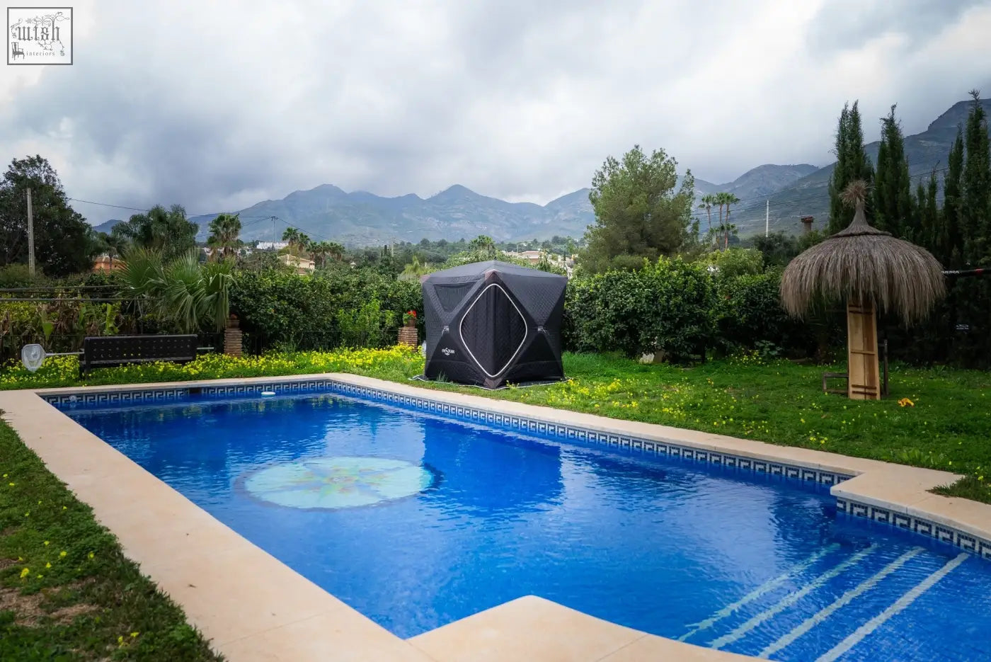 Rectangular blue swimming pool with tiled edges and thatched umbrella near noir xxl r14s second tent sauna suite with safety pack
