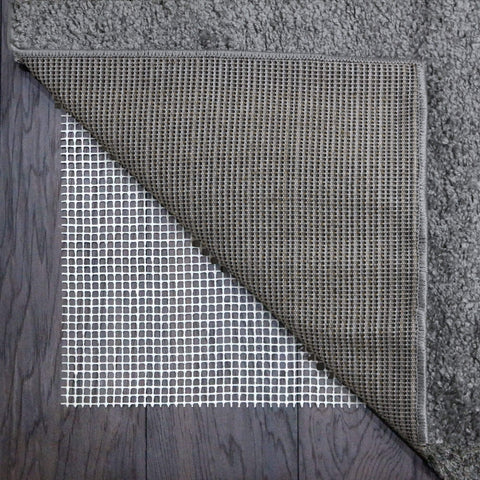 Gray textured rug showing woven backing with white non slip adhesive grid of rug gripper underlay visible beneath corner