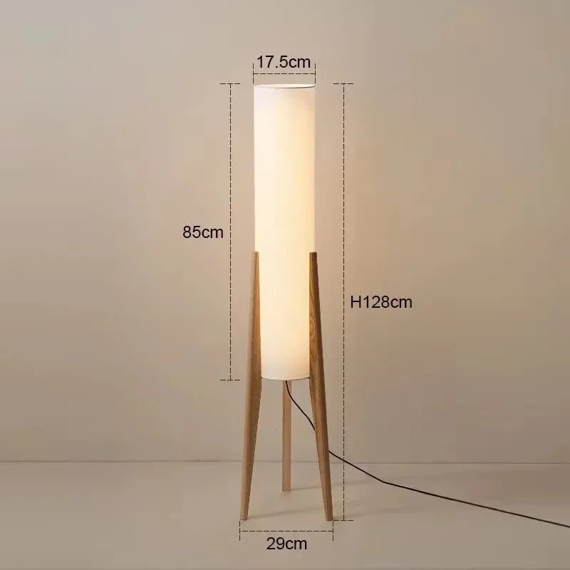 A tall nordi light floor lamp with warm white light and a translucent fabric shade on slender wooden legs