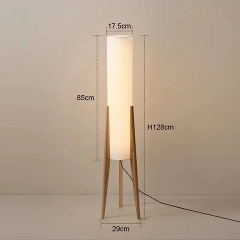 A tall nordi light floor lamp with warm white light and a translucent fabric shade on slender wooden legs