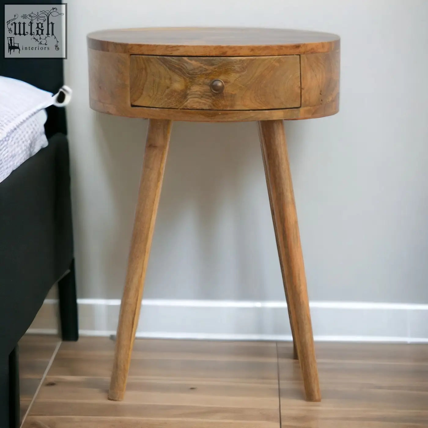 A nordic circular shaped bedside table made of oak mango wood with a single drawer and tapered legs in natural finish