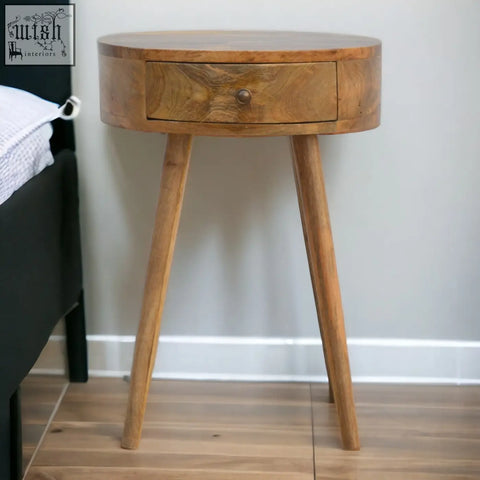 A nordic circular shaped bedside table made of oak mango wood with a single drawer and tapered legs in natural finish