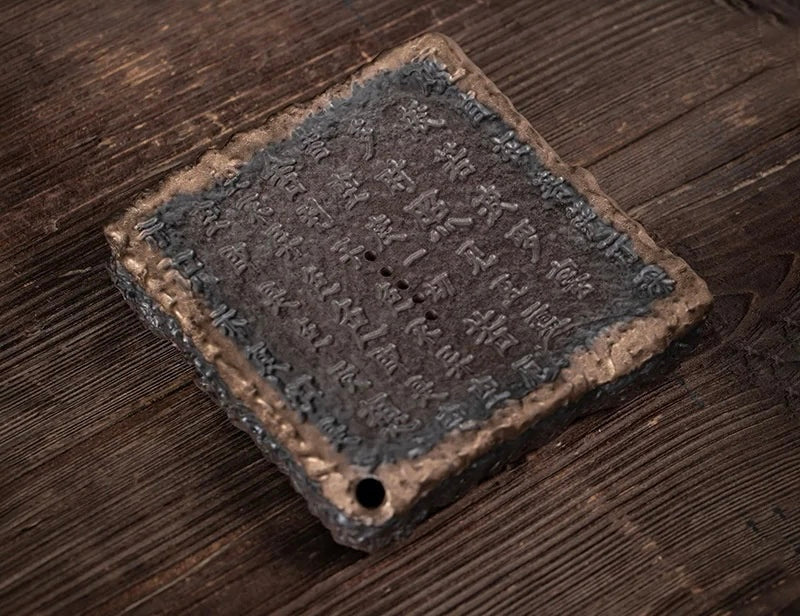 A weathered bronze plaque with engraved chinese characters on the back of an ocha tea set