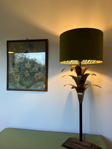 A tall table lamp with an olive green velvet cylindrical shade and ornate metallic palm leaf base for stylish lighting
