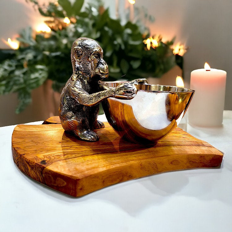 Shiny metallic monkey figurine holding a reflective gold bowl on an olive wood base rustic serving board