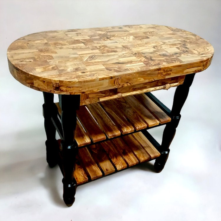 Oval-shaped olive wood butcher block kitchen island with mosaic top and slatted shelves with dark turned legs