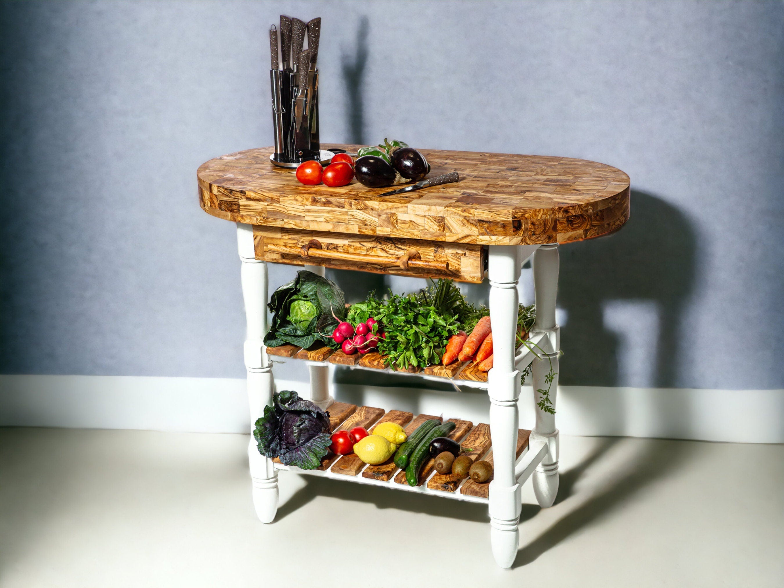 Rustic oval kitchen cart with white legs and shelves featuring an olive wood butcher block top and fresh produce storage