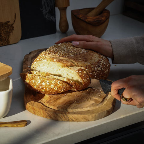 A golden-brown artisan loaf on a crusty olive wood carving board with groove perfect for wood carving use