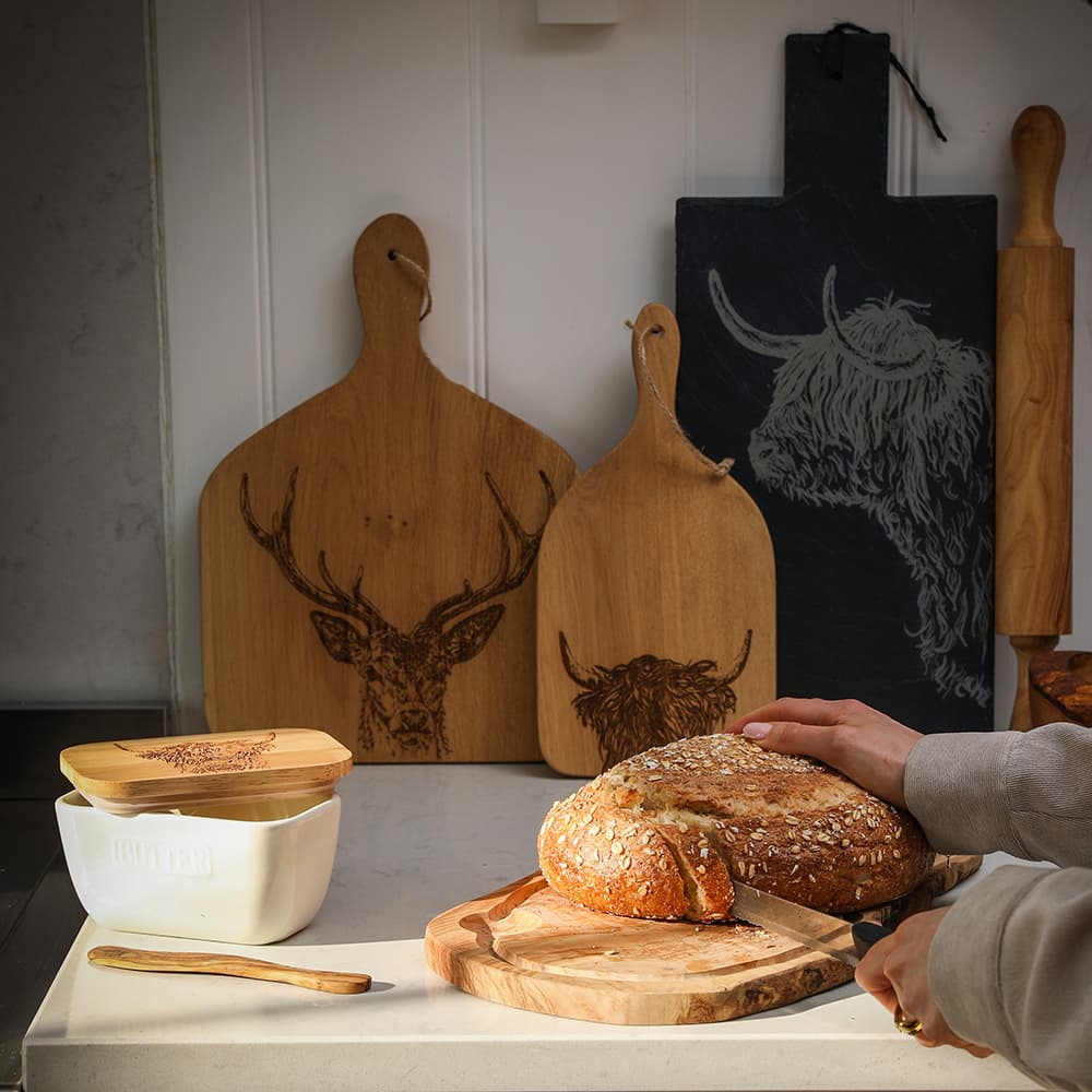 Rustic light brown olive wood carving board with natural edge groove and hand carved highland cow design
