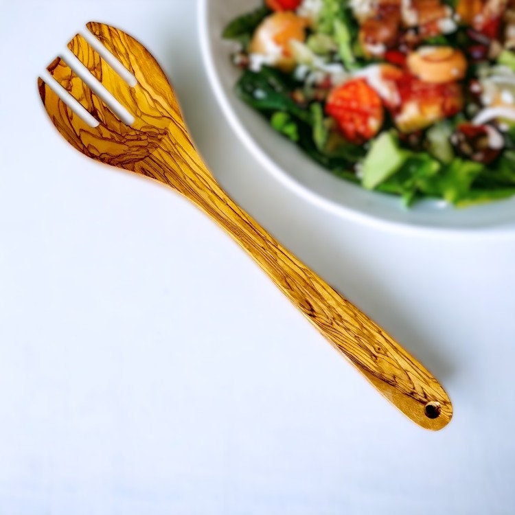 A golden-hued olive wood salad server with natural grainy texture and three slots from olive trees story utensil set