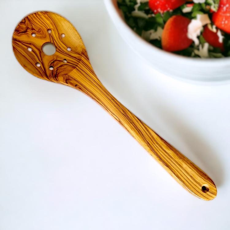 A wooden olive wood slotted spoon with a warm golden-brown finish and dark streaks from olive trees story