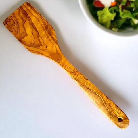 Olive wood spatula with polished warm golden amber tones and natural swirling grain from the olive tree story