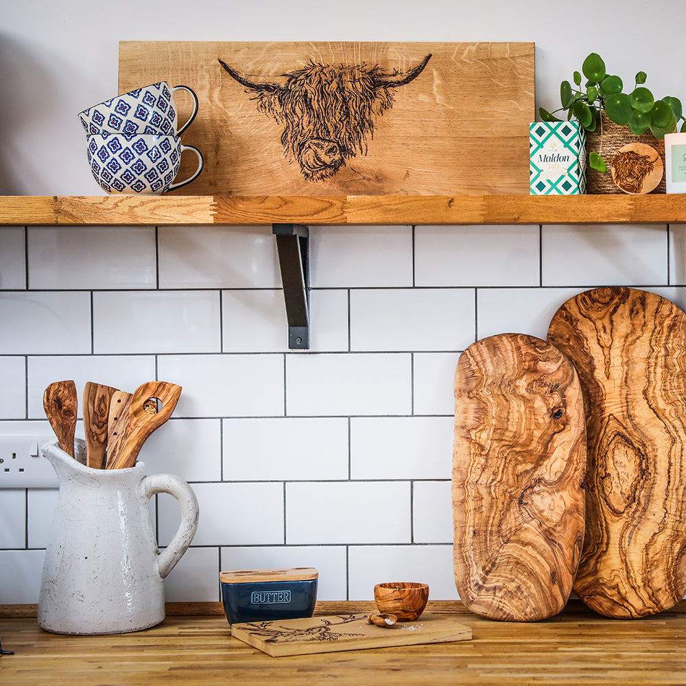 Two rustic olive wood corner spoons with swirling grain patterns resting on a wooden countertop