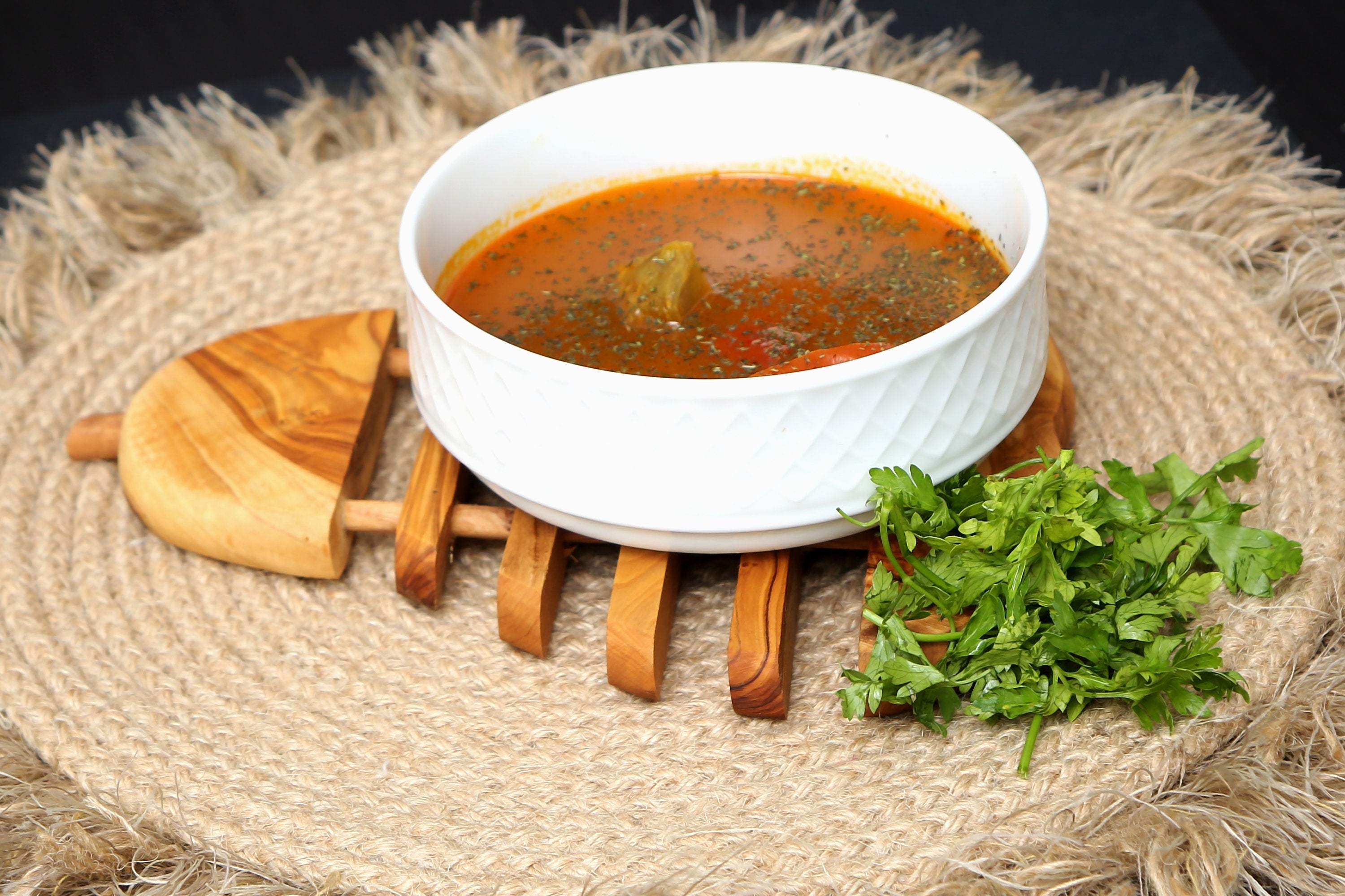 A white ceramic bowl of orange-red soup on a 21 cm olive wood pear pan coaster serving as a stylish pan coaster