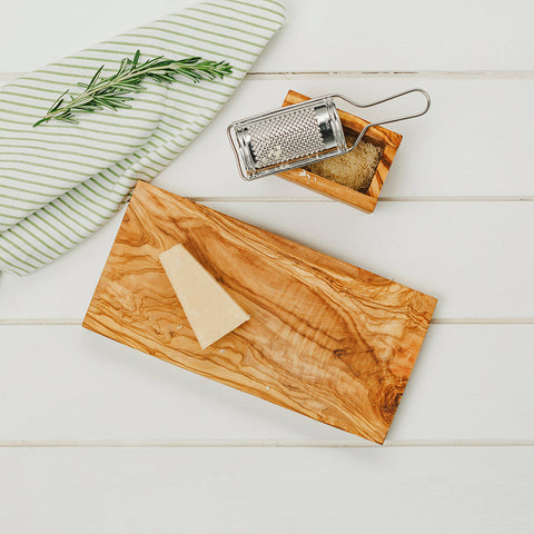 Rectangular olive wood chopping board with natural grain and warm golden-brown tones holding a wedge of cheese