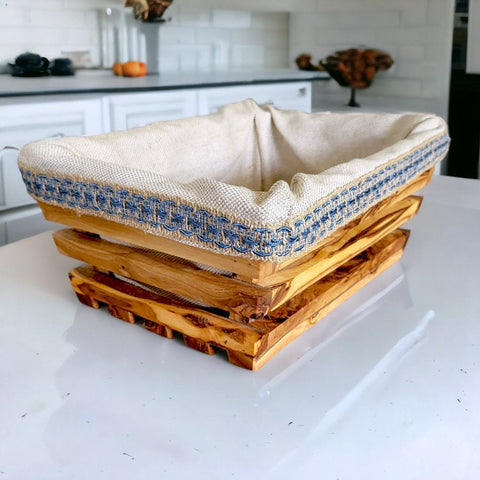 A rustic olive wood bread basket with a beige linen-lined interior and blue embroidered trim 28 cm rectangular shape