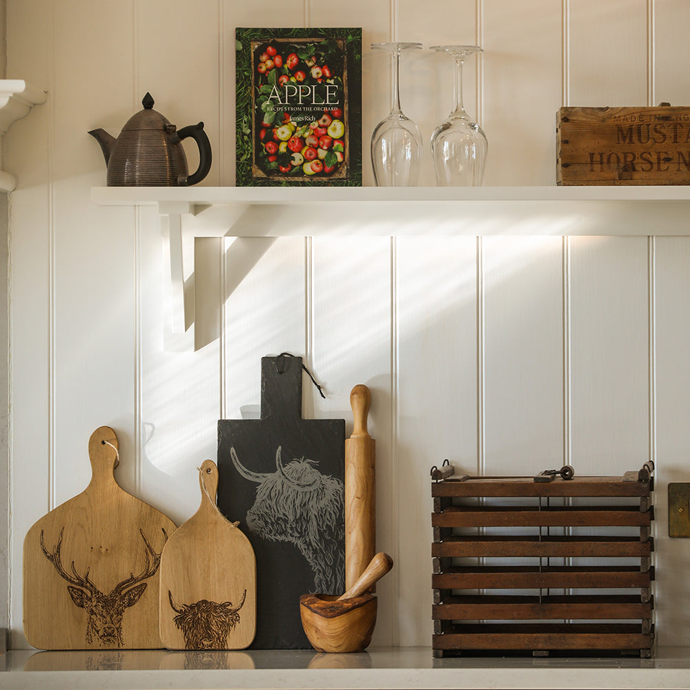 Dark gray slate cutting board with engraved highland cow design shown alongside olive wood rolling pin for baking use