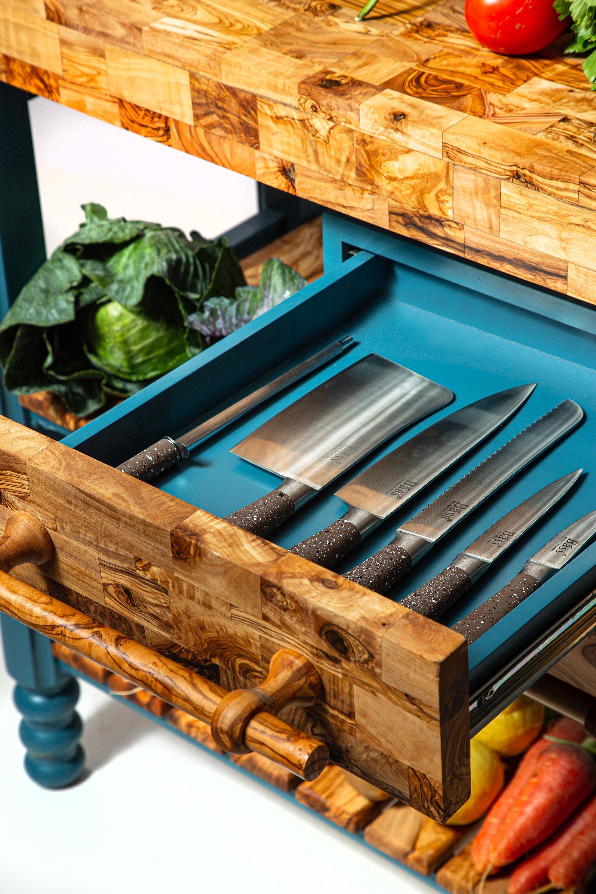 Set of five stainless steel knives with dark wood handles neatly arranged in a wooden drawer of olive wood table butcher block