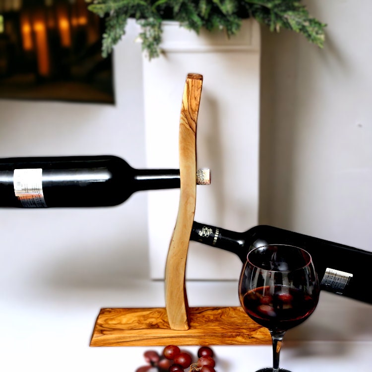 A sleek olive wood bottle holder with a curved design and natural grain perfect for wine or barware gifts