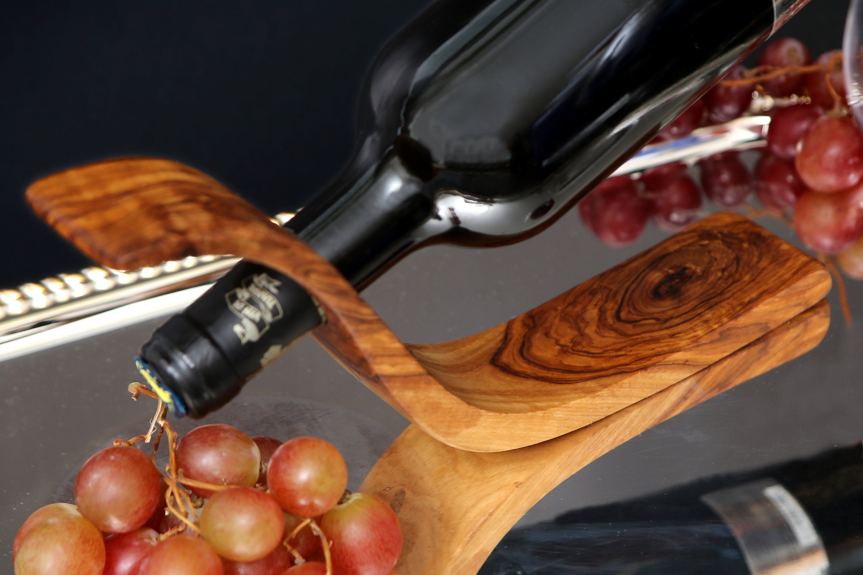 A dark glass wine bottle resting on a handcrafted olive wood wave bottle holder with swirling grain patterns