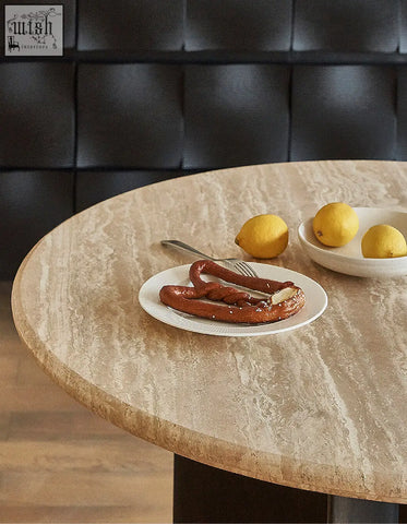A golden brown pretzel on a white plate sits on the travertin and solid wood oval dining table from o malley