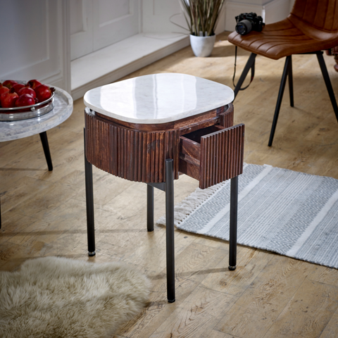 A sleek oval mango wood bedside table with a white marble top and textured dark wood body with vertical grooves
