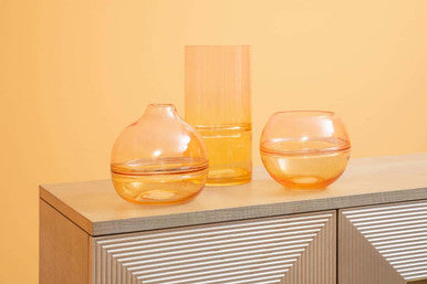 Three amber-colored glass optik bottle vases of varying shapes sitting on a modern cabinet