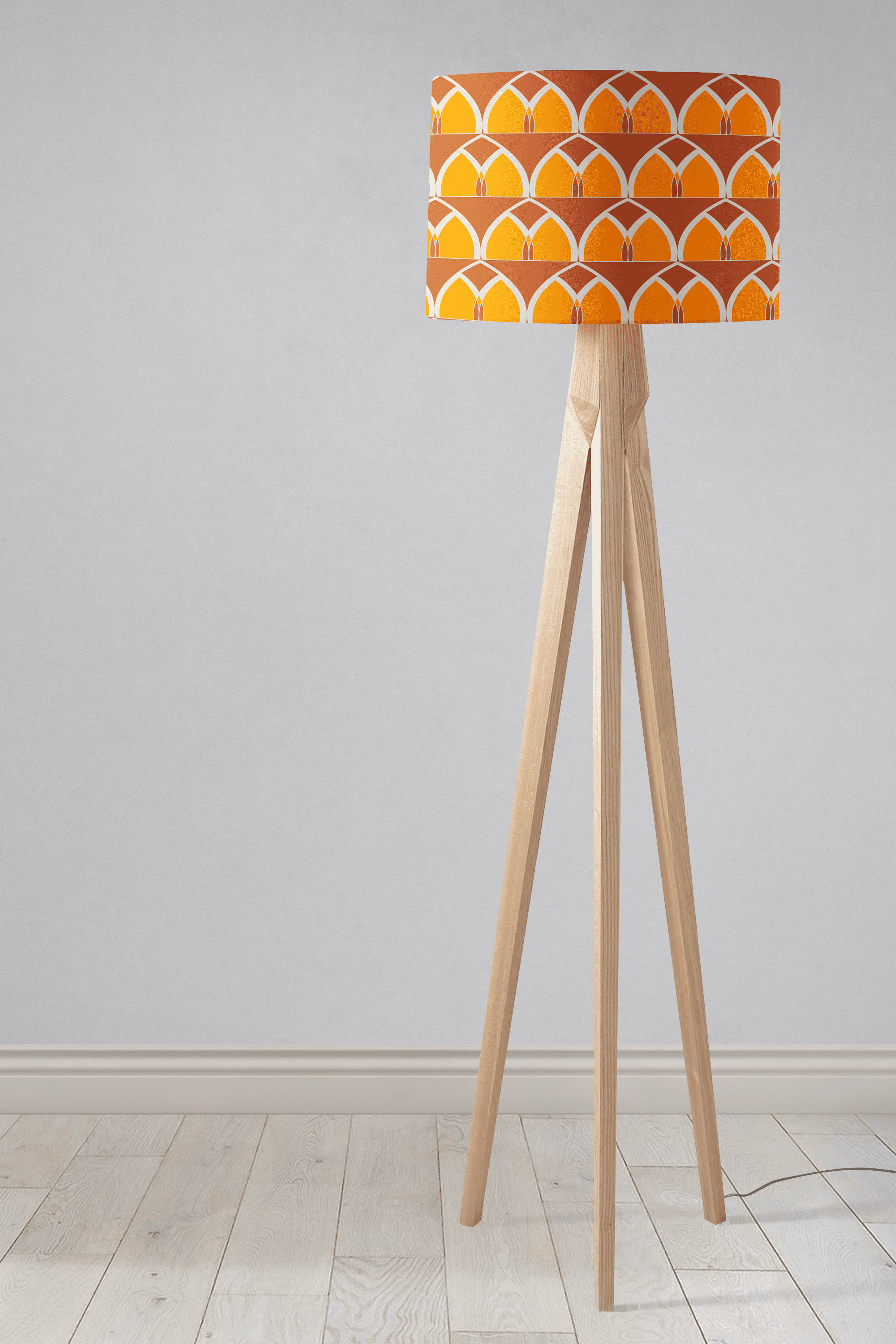 A modern tripod floor lamp with an orange and yellow geometric arches patterned table lamp shade