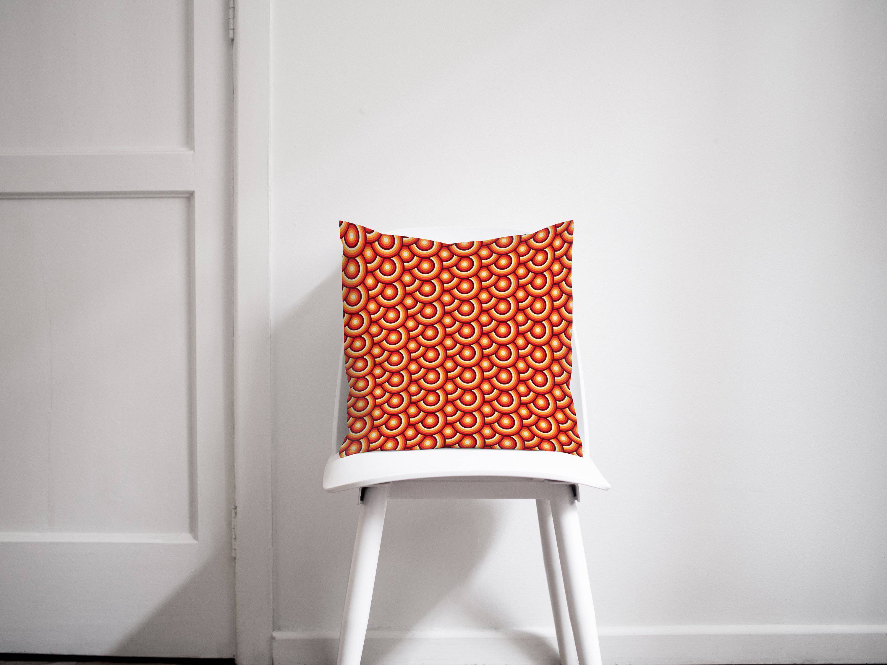 Vibrant orange throw pillow with 70s retro circles design resting on a white chair for cozy home decor