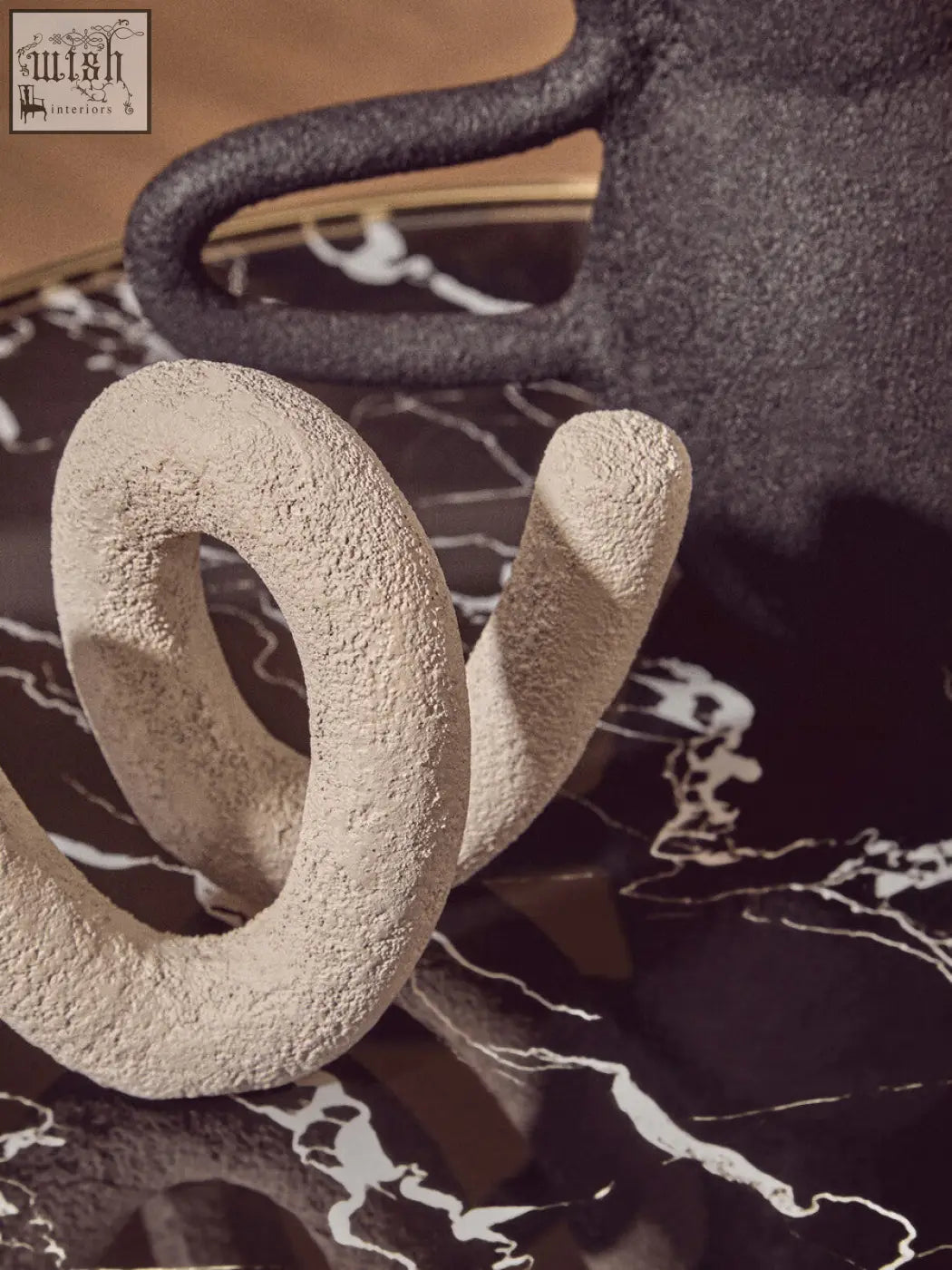 Cream-colored textured ceramic sculpture with sculpted loop and curved form on oria black glass marble base side table