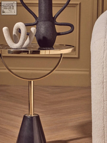 A sleek oria black glass side table with a polished gold top and marble base supported by a slim brass stem