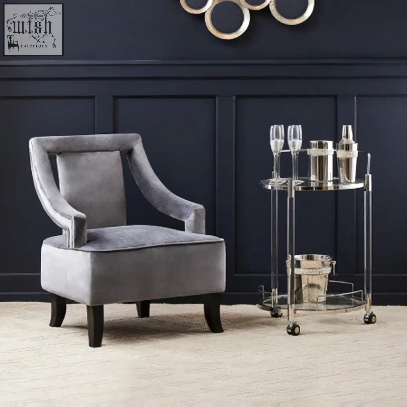 Gray velvet armchair with curved arms and dark wooden legs next to oria round 2 tier drinks trolley for stylish tier drinks storage