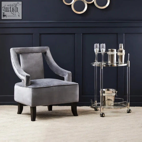 Gray velvet armchair with curved arms and dark wooden legs next to oria round 2 tier drinks trolley for stylish tier drinks storage