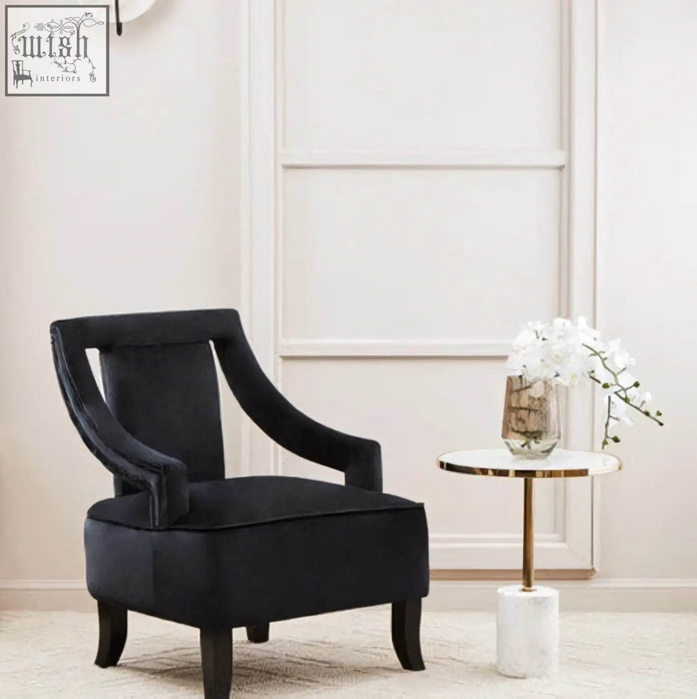 Black velvet armchair with curved wooden legs next to a sleek oria white marble end table with stainless steel base