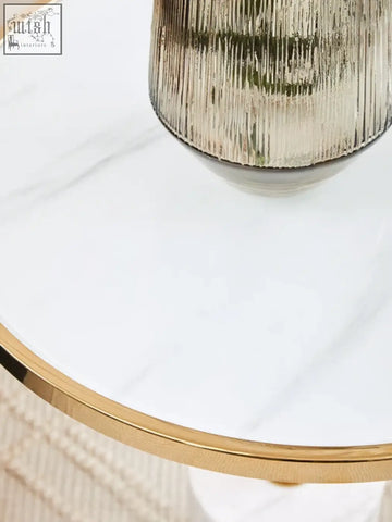 A sleek metallic gold vase with a ribbed texture on a white marble end table with stainless steel legs