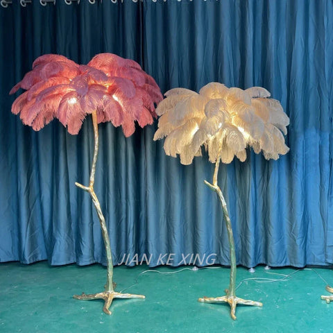Two ostrich feather floor lamps with pink and cream feathery tops on gold branch stems perfect for living room decor