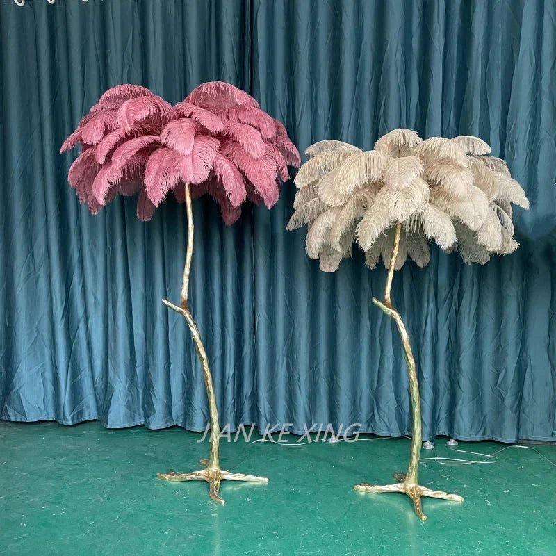 Two ostrich feather floor lamps in soft pink and cream with golden branch bases perfect for living room decor