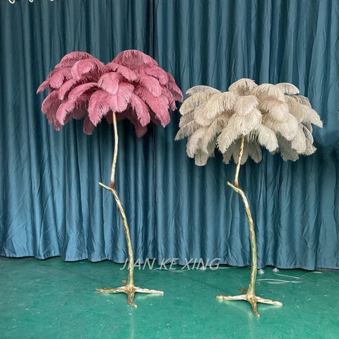 Two ostrich feather floor lamps in soft pink and cream with golden branch bases perfect for living room decor